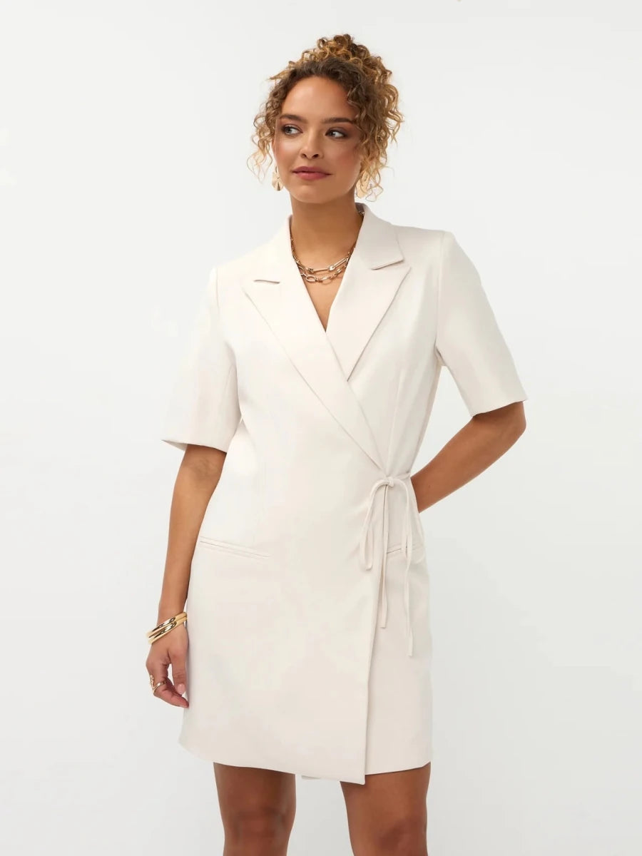 Een model met opgestoken krullend haar presenteert een gebroken witte blazerjurk met korte mouwen | Ydence Hazel | Jo&Co Club