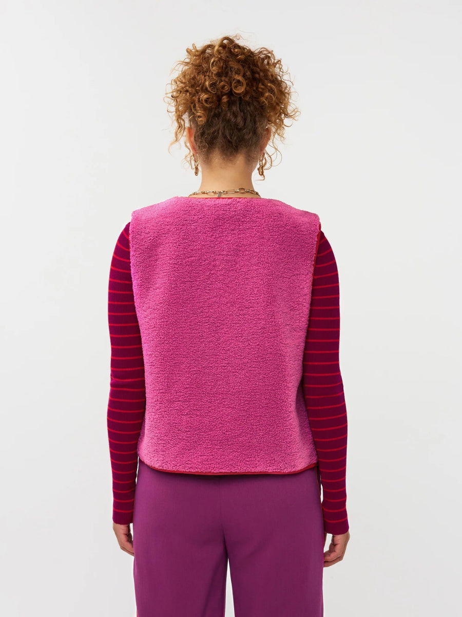 Model draagt het puck gilet van ydende van teddy stof in de kleur fuchsia over de knitted top devina.