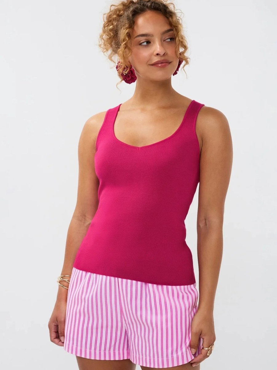 Model draagt de Ydence top Leny, een mouwloze gebreide top in felroze kleur, gestyled met een gestreepte short.
