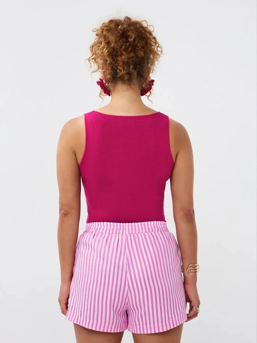 Model draagt de Ydence top Leny in felroze zomerse stijl met een roze-wit gestreepte short, achteraanzicht.