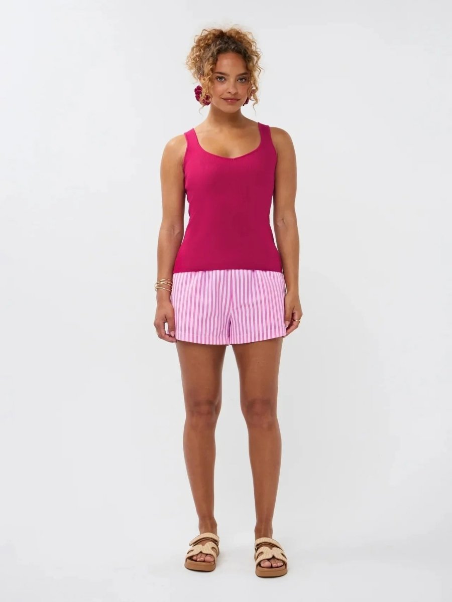 Model draagt de Ydence top Leny, een felroze gebreide mouwloze top gecombineerd met een roze-wit gestreepte short.
