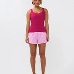 Model draagt de Ydence top Leny, een felroze gebreide mouwloze top gecombineerd met een roze-wit gestreepte short.