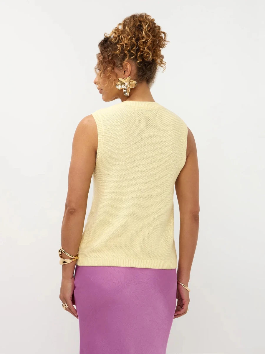 Een model, van achteren gefotografeerd, draagt een mouwloze, pastelgele gebreide top met een | Ydence Mona | Jo&Co Club