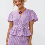 Model draagt de larissa short en de Milay top, een broderie wikkelblouse met korte mouwen en strikceintuur van Ydence.