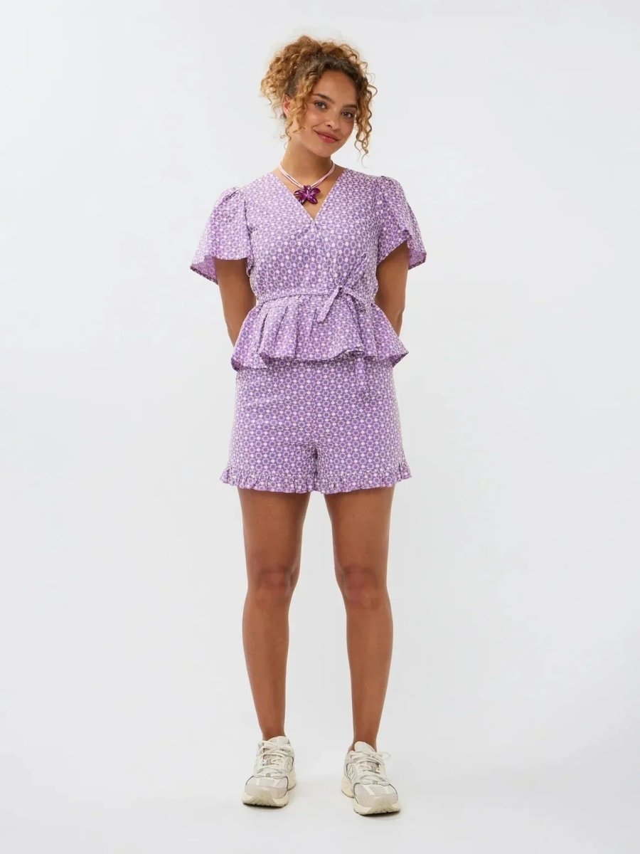 Model draagt de Ydence Milay top en Larissa short, een paarse co-ord set in broderie stijl met bloemmotief en ruches.