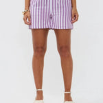 Model draagt de Mima short, een lila-wit gestreepte linnen short met strikceintuur van Ydence.