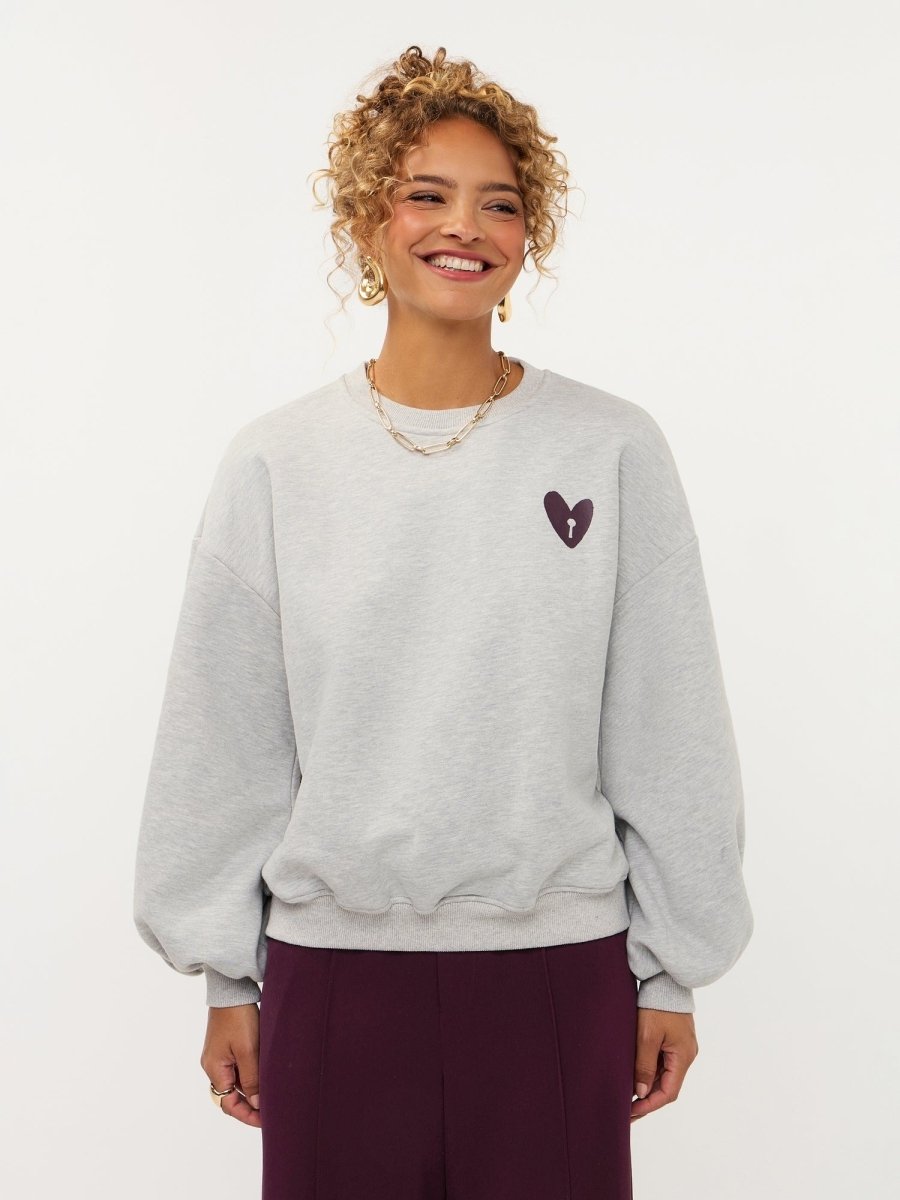Model in grijze sweater met hartje en print op de rug Ydence Checked In | Jo&Co Club
