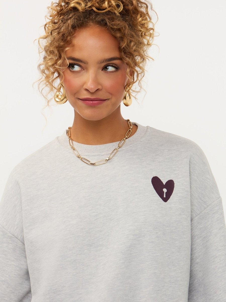 Campagnebeeld Ydence winter 2026: grijze sweater met hartje en print op de rug Ydence Checked In | Jo&Co Club