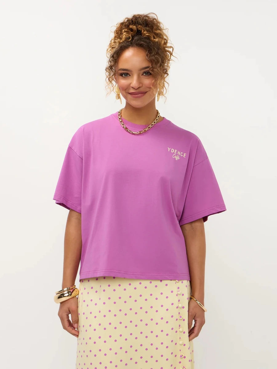 Een model met opgestoken krullend haar presenteert een oversized fuchsia T-shirt met een kleine | Ydence cafe | Jo&Co Club