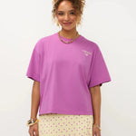 Een model met opgestoken krullend haar presenteert een oversized fuchsia T-shirt met een kleine | Ydence cafe | Jo&Co Club