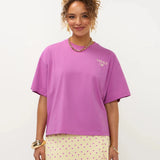 Een model met opgestoken krullend haar presenteert een oversized fuchsia T-shirt met een kleine | Ydence cafe | Jo&Co Club