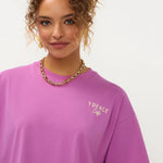 Een close-up portret van een model met krullend, opgestoken haar, die een paars T-shirt met een | Ydence cafe | Jo&Co Club