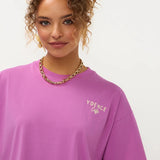 Een close-up portret van een model met krullend, opgestoken haar, die een paars T-shirt met een | Ydence cafe | Jo&Co Club
