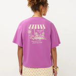 Een model, van achteren gefotografeerd, draagt een oversized magenta T-shirt tegen een witte | Ydence cafe | Jo&Co Club