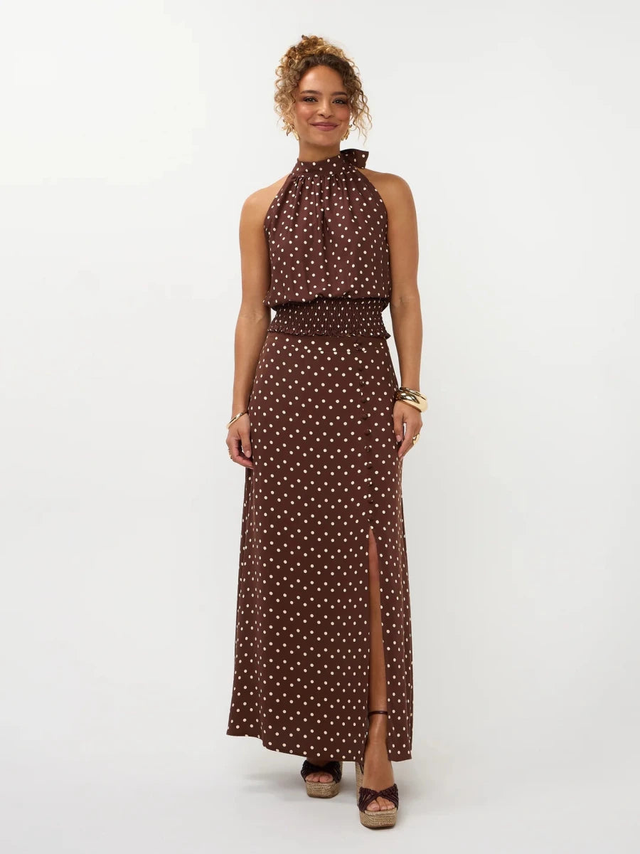 Een model poseert in een lange, bruine halterjurk met een crèmekleurige polkadotprint | Ydence Jamie | Jo&Co Club