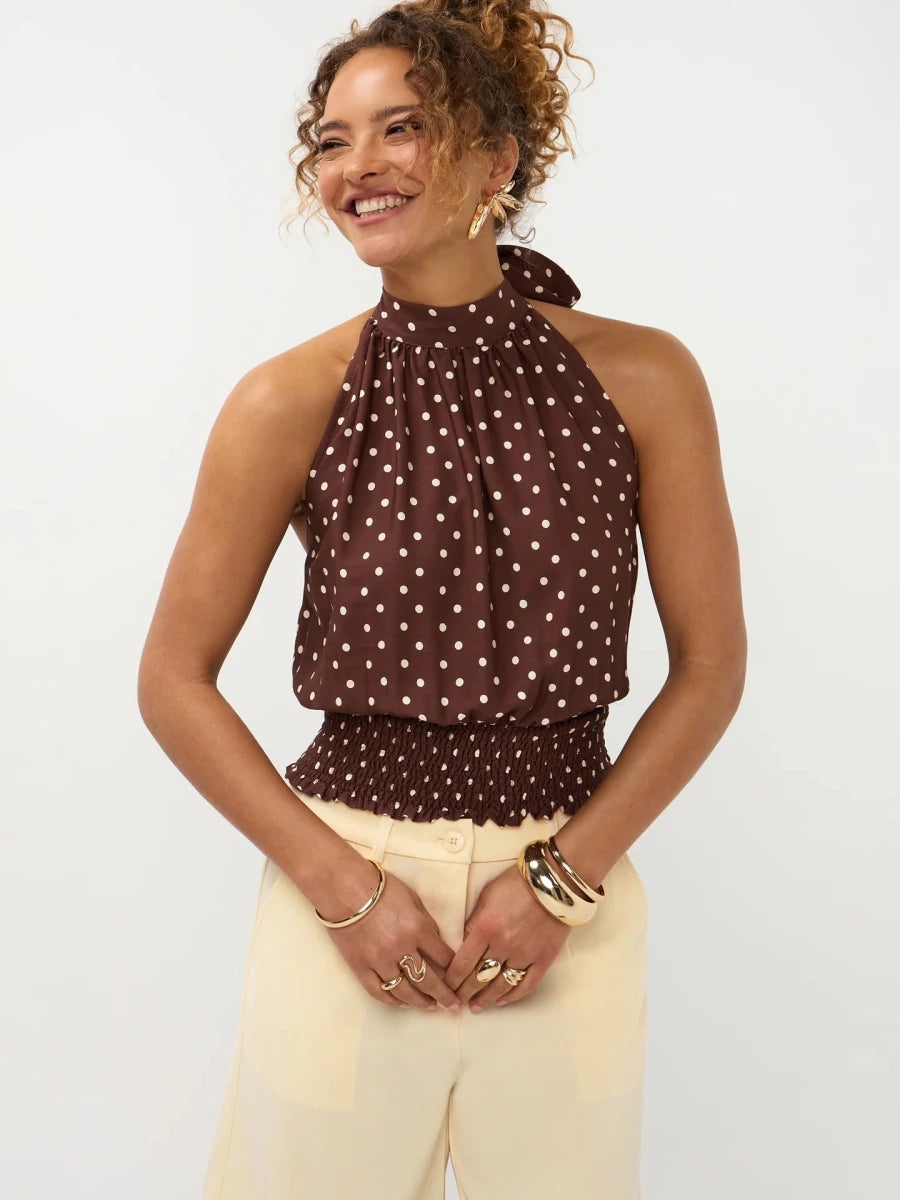 Een model met een vrolijke lach draagt een bruine haltertop met witte polkadots | Ydence Jamie | Jo&Co Club