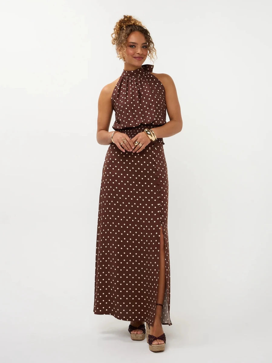 Een model met opgestoken krullend haar poseert in een donkerbruine maxi-jurk met een | Ydence Jamie | Jo&Co Club